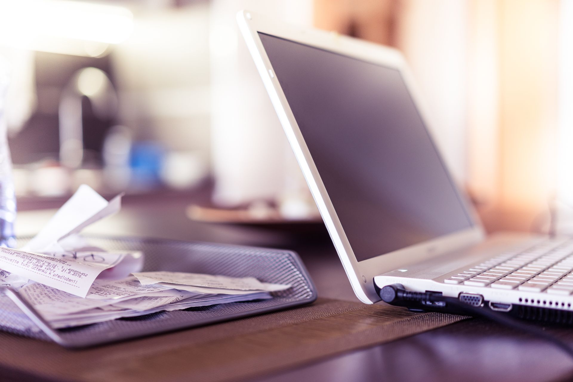 Laptop beside a tray of paper receipts on a desk